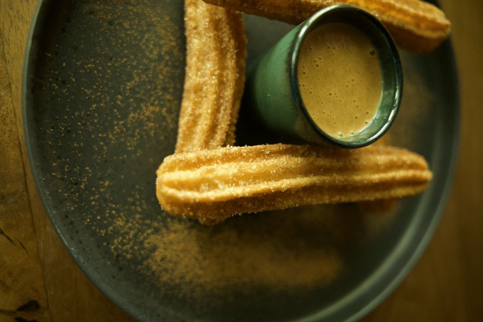 Churros with cinnamon sugar and a small bowl of dip on a dark plate.