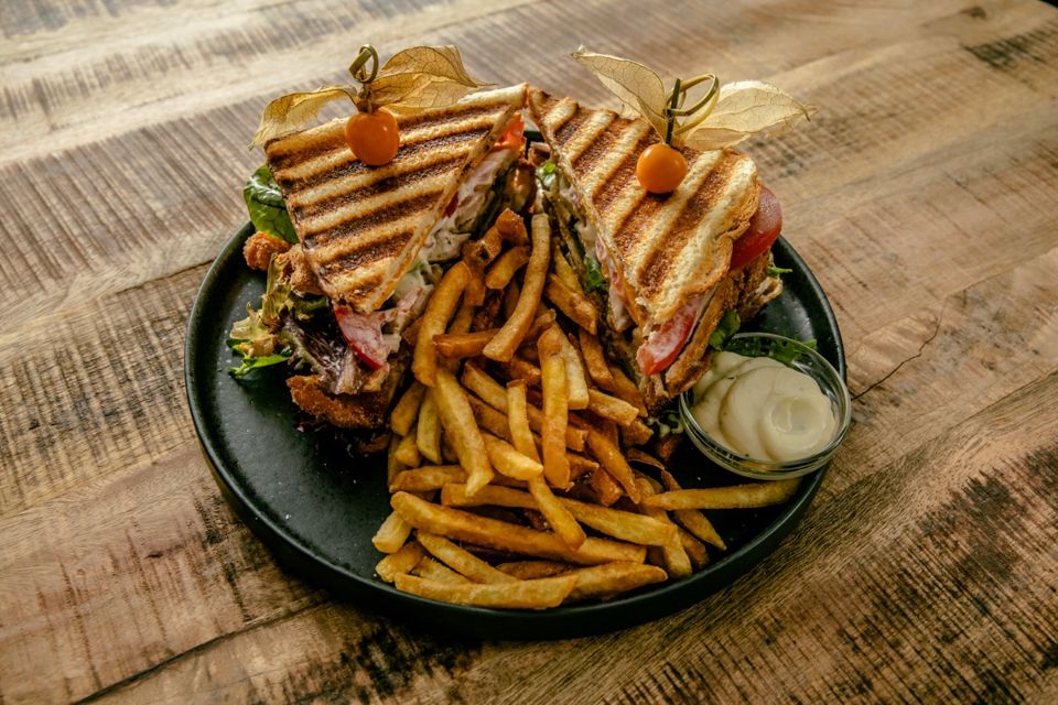 Club sandwich with fries and dip on a wooden table.