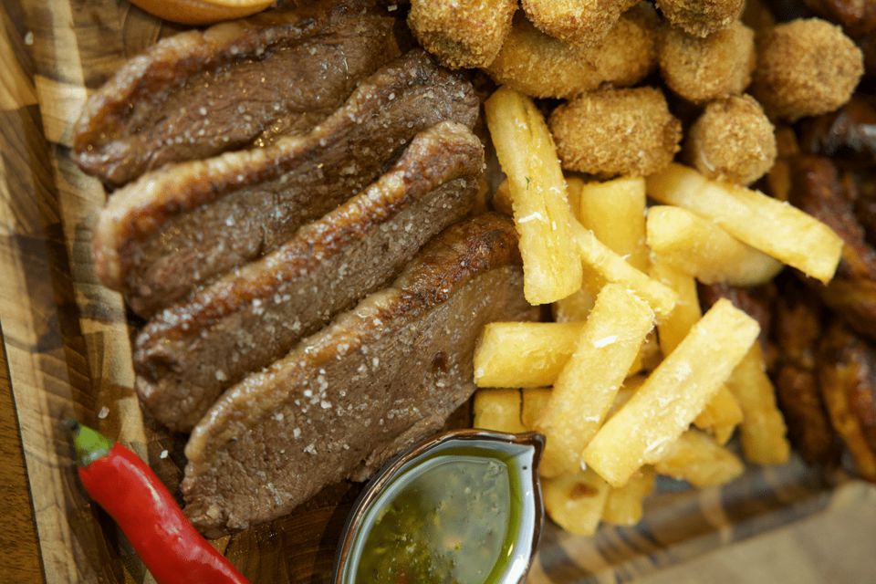 Sliced picanha with fries, cassava balls and green sauce on a wooden board.