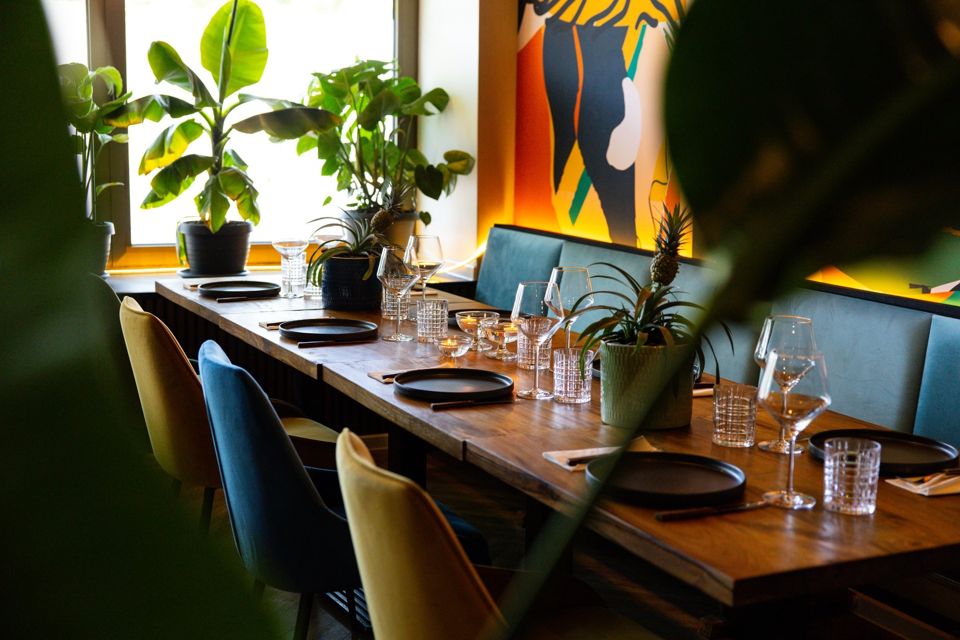 The Baioca dining room: long wooden tables, blue upholstered benches, plants at the window and a colourful mural.