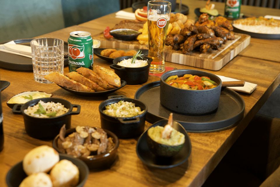 A generously laid wooden table at Baioca with many small bowls of Brazilian petiscos, bread and drinks.